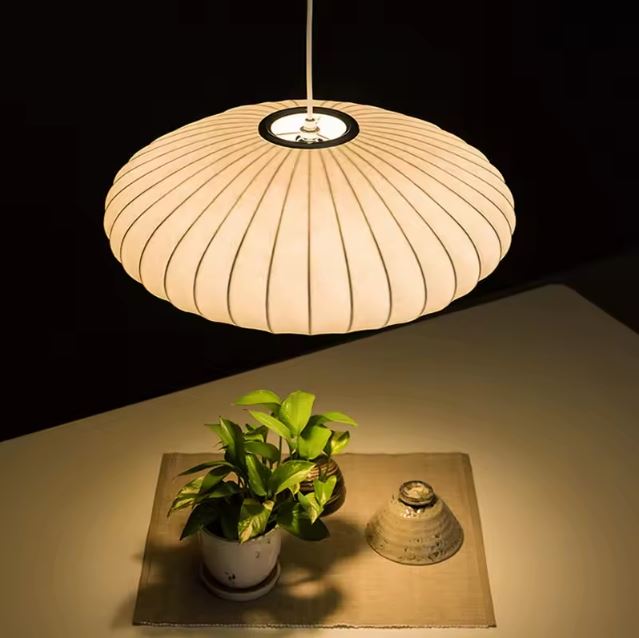 Suspension japonaise en tissu de soie diffusant une lumière chaude au-dessus d’une table décorée de façon zen.
