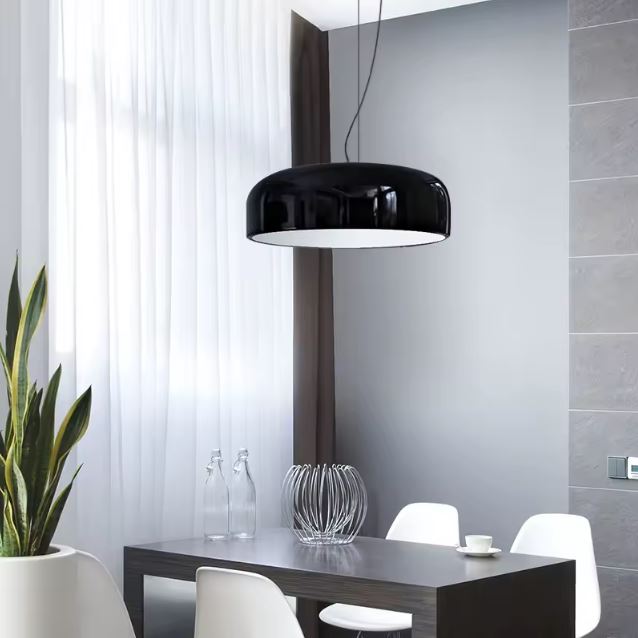 Suspension ronde noire brillante au style minimaliste, suspendue au-dessus d'une table moderne dans une salle à manger épurée.