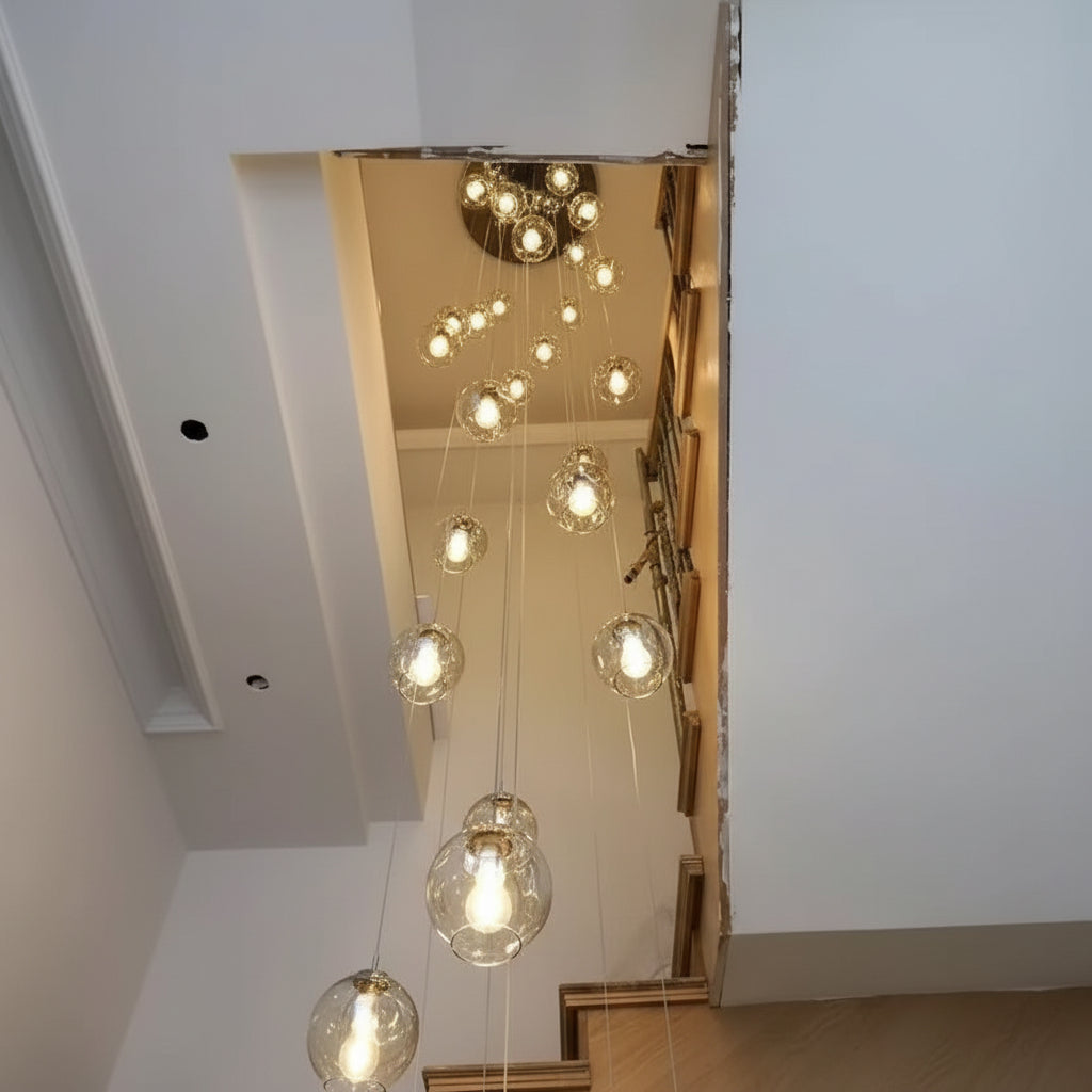 Grande suspension cascade composée de multiples globes en verre transparent suspendus à différentes hauteurs dans une cage d'escalier moderne à plafond haut, diffusant une lumière chaleureuse et élégante
