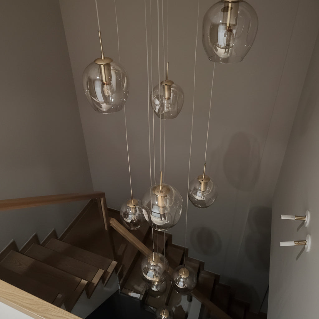 Suspension cascade composée de plusieurs globes en verre transparent suspendus à différentes hauteurs au-dessus d'un escalier moderne avec finitions en laiton doré