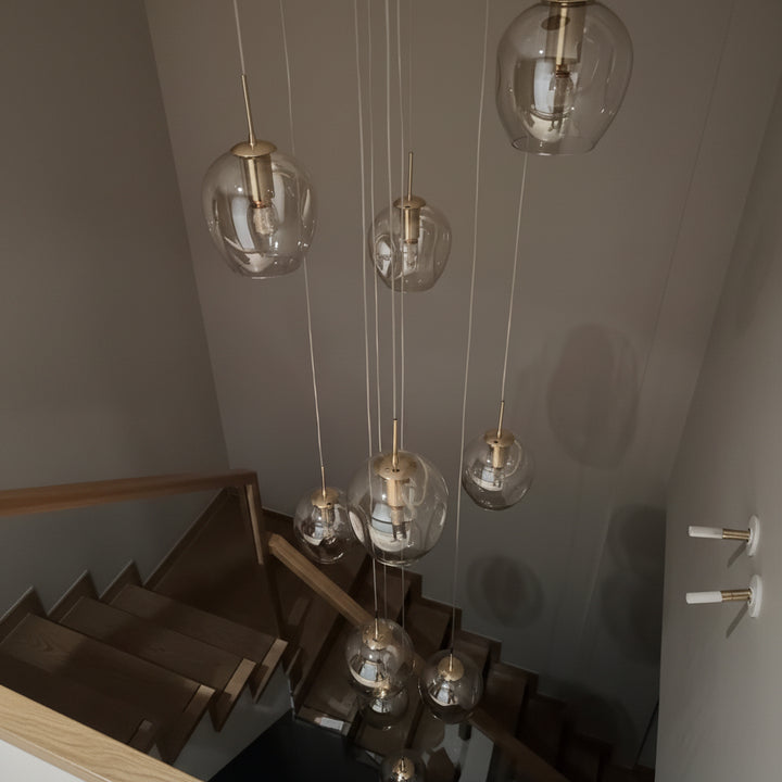 Suspension cascade composée de plusieurs globes en verre transparent suspendus à différentes hauteurs au-dessus d'un escalier moderne avec finitions en laiton doré