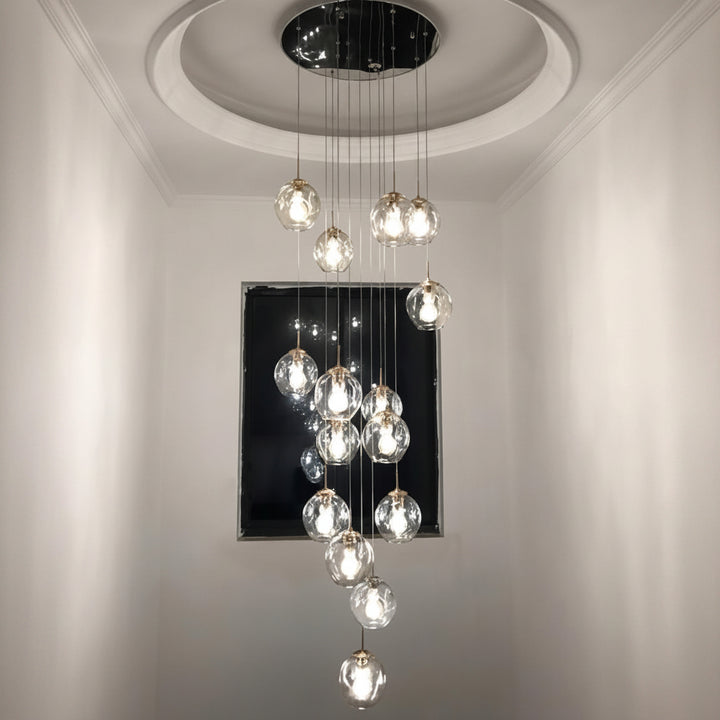 Suspension moderne composée de globes en verre transparent suspendus à différentes hauteurs dans une entrée avec plafond haut