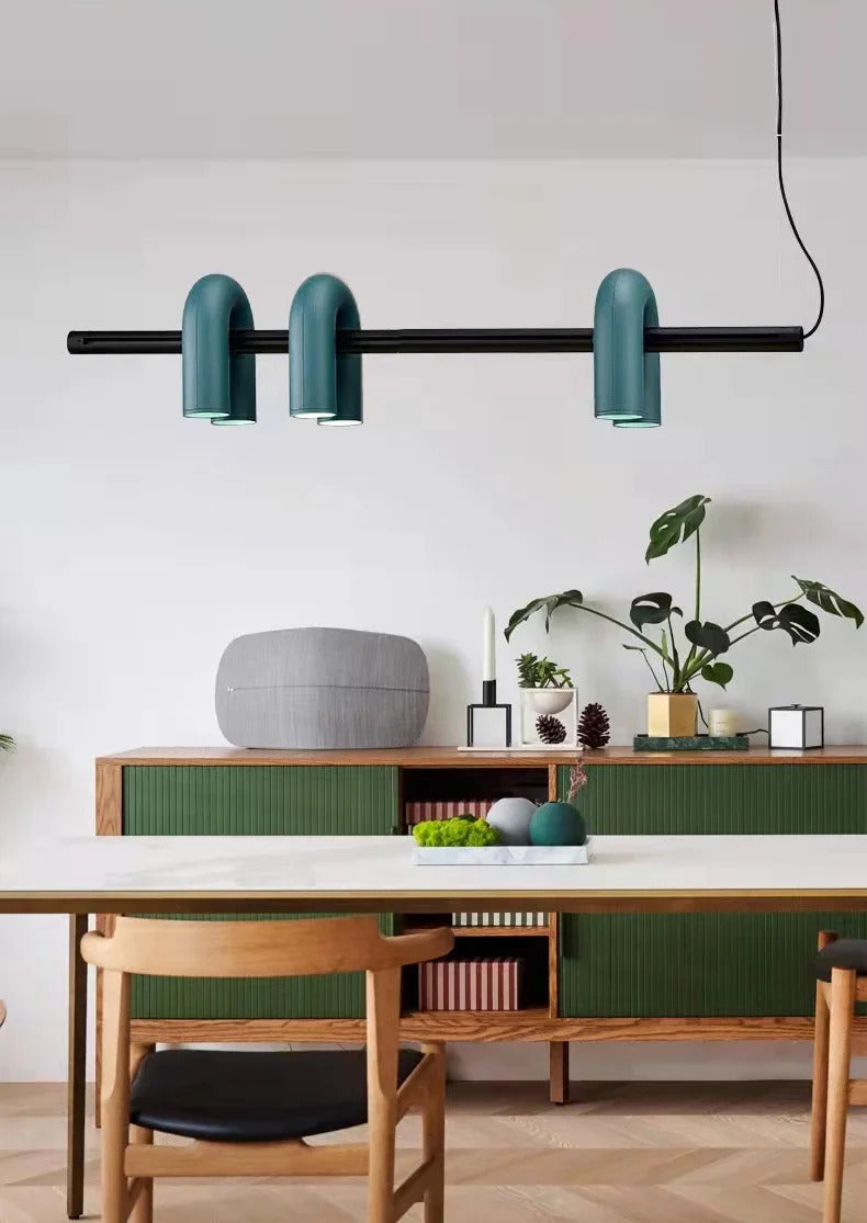 Suspension design tubulaire aux courbes en U en finition bleu installée au-dessus d'une table moderne, apportant un éclairage élégant et une touche contemporaine à l'espace.