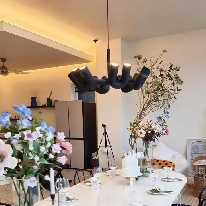 Suspension design tubulaire aux courbes en U en finition noir mat installée au-dessus d'une table à manger, créant un éclairage moderne et une ambiance élégante.