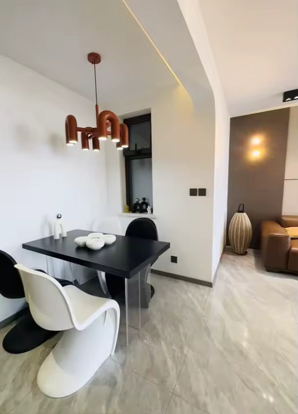 Suspension design tubulaire aux courbes en U en finition orange installée au-dessus d'une table de repas moderne, apportant un éclairage chaleureux et une touche contemporaine à l'espace.