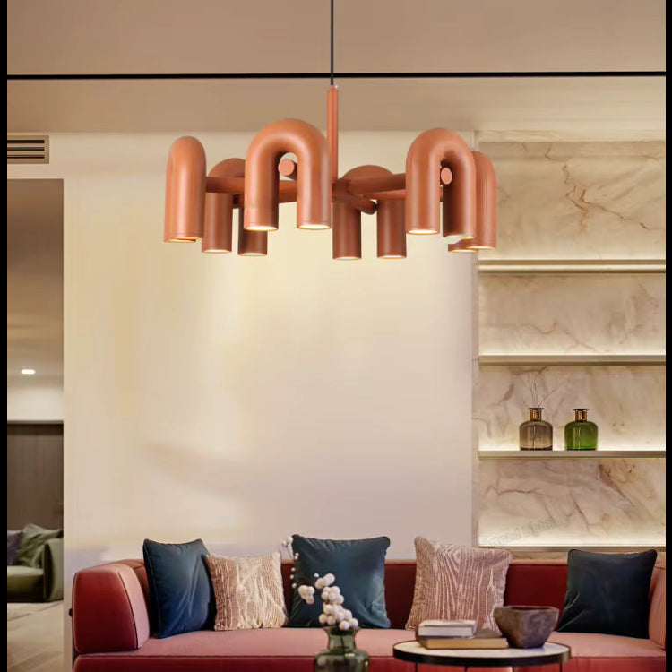 Suspension design tubulaire aux courbes en U en finition orange installée au-dessus d'un salon moderne, créant un éclairage chaleureux et une ambiance contemporaine.