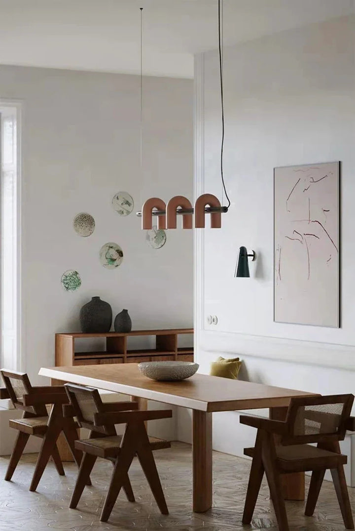Suspension design tubulaire aux courbes en U en finition orange installée au-dessus d'une table de salle à manger moderne, apportant une touche contemporaine et chaleureuse à l'espace.