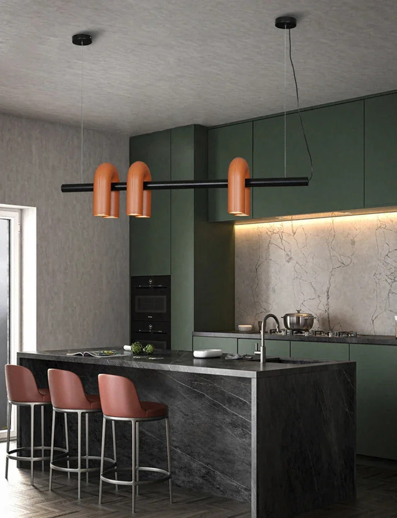 Suspension design tubulaire aux courbes en U en finition orange installée au-dessus d'une table à manger, créant un éclairage chaleureux et une ambiance moderne dans la salle à manger.