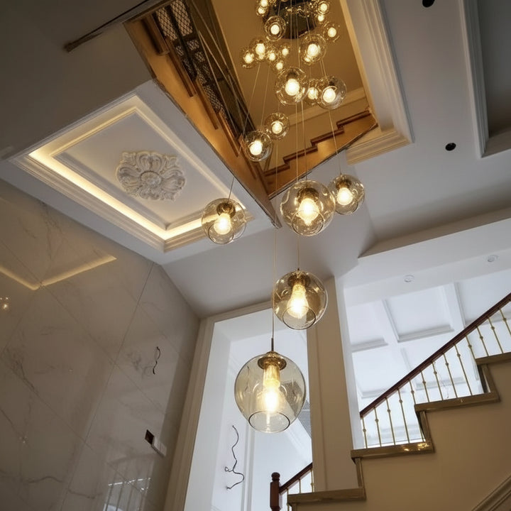 Suspension design en cascade avec globes en verre transparent suspendus dans une cage d'escalier moderne à grande hauteur sous plafond.
