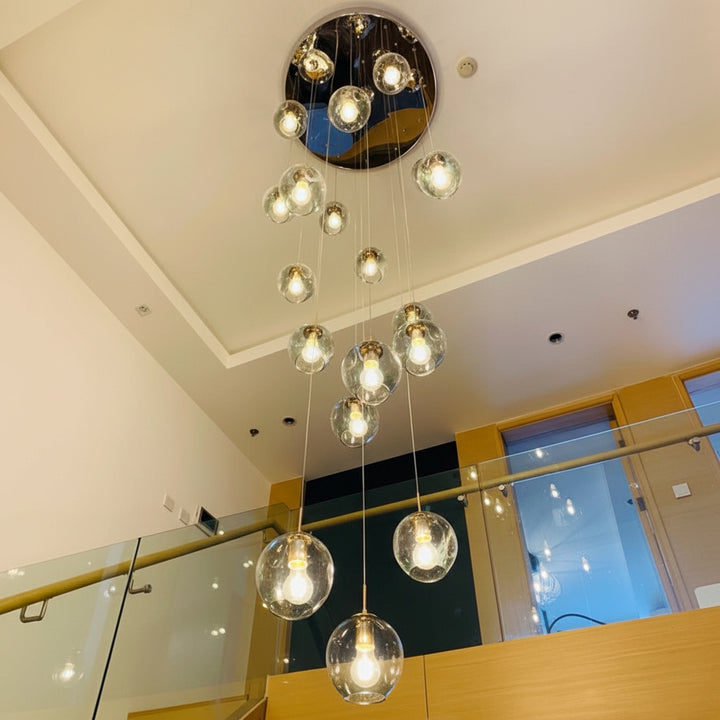 Ensemble de suspensions en verre transparent disposées en cascade dans un espace ouvert avec escalier et plafond double hauteur