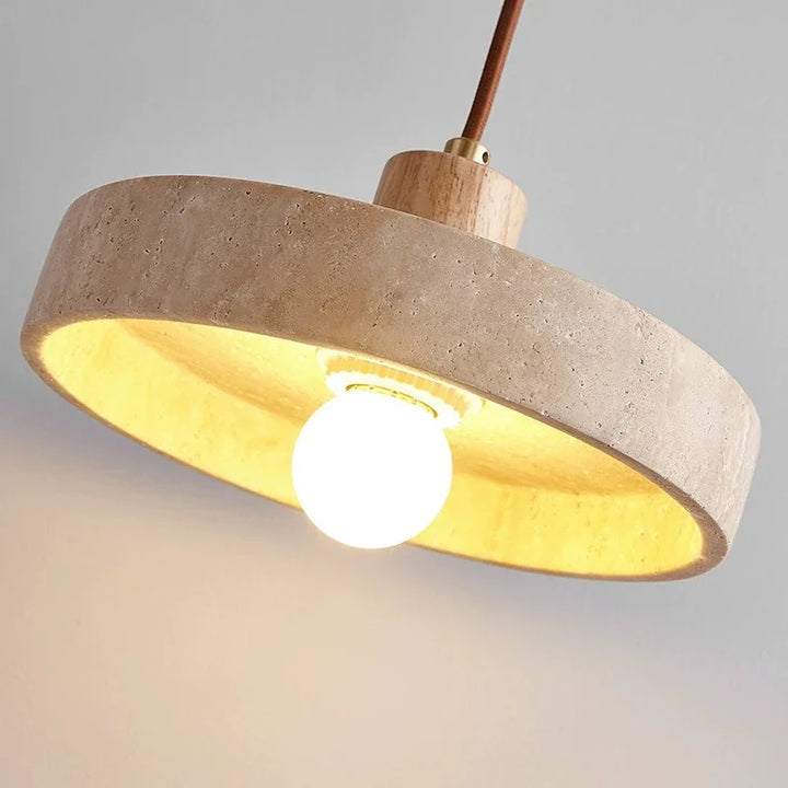 Gros plan sur l'abat-jour cylindrique en travertin claire d'un luminaire suspendu au style contemporain.
