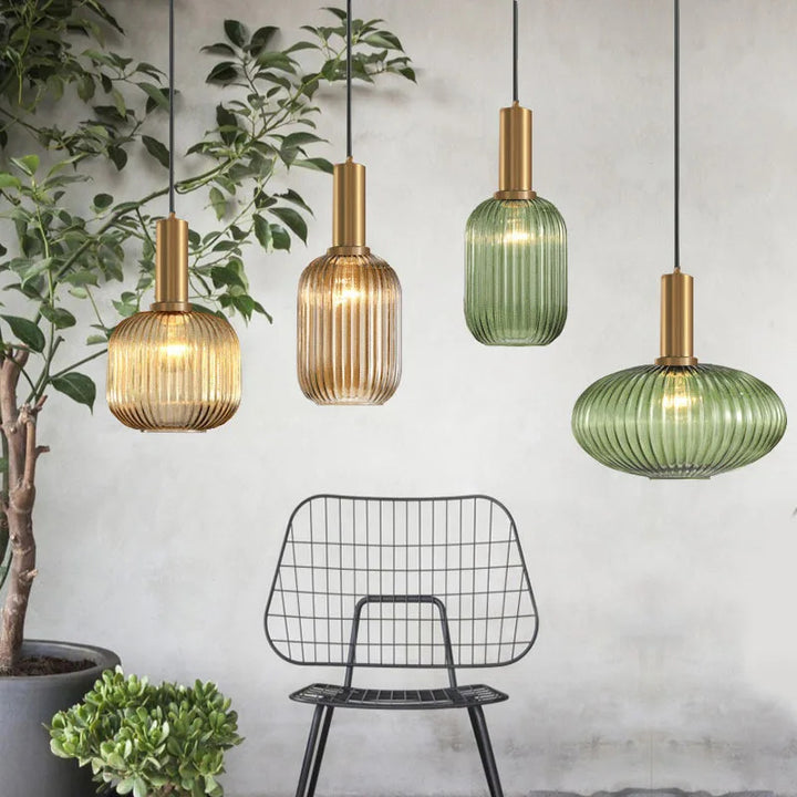 Collection de suspensions en verre cannelé vert et ambré avec finitions dorées, suspendues dans un intérieur moderne. Ces luminaires décoratifs apportent élégance, chaleur et caractère à l’espace de vie.