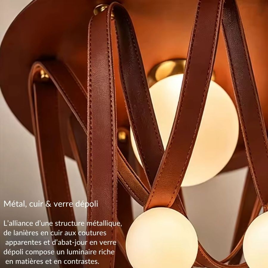 Gros plan sur les lanières de cuir cousues et les globes en verre dépoli d’un luminaire sculptural et chaleureux.