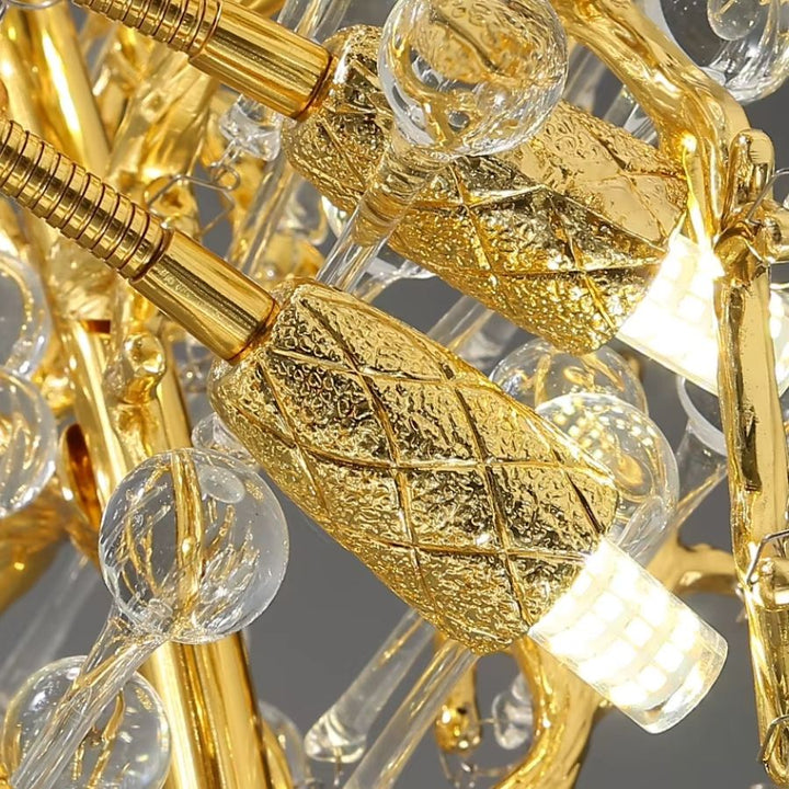 Gros plan sur la finition dorée ouvragée et la source lumineuse intégrée au cœur du lustre à pampilles de cristal