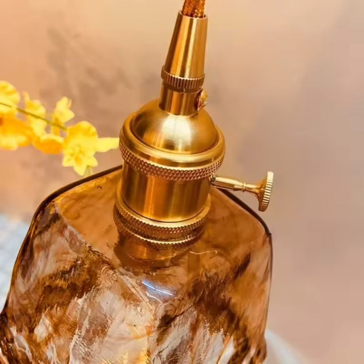 Gros plan sur la douille dorée rétro et le verre ambré sculpté d’une suspension au charme vintage raffiné