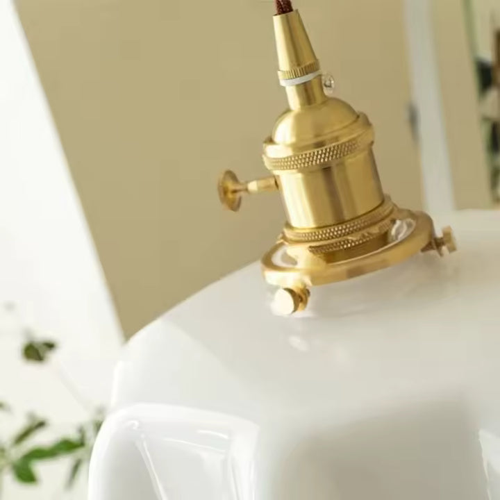 Gros plan sur la douille en laiton d’une suspension vintage à abat-jour festonné blanc au charme rétro