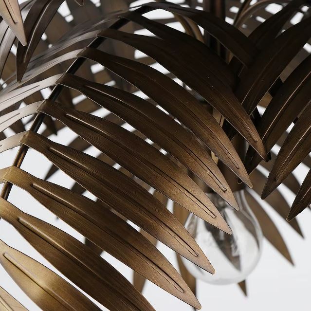 Détail des feuilles en métal cuivré de la suspension palmier, laissant entrevoir l’ampoule pour un rendu tropical raffiné.