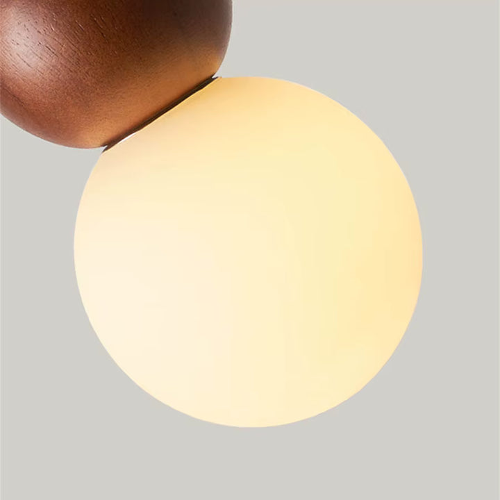 Gros plan sur le globe opalin lumineux et la sphère en bois d’une suspension totem au design organique et épuré