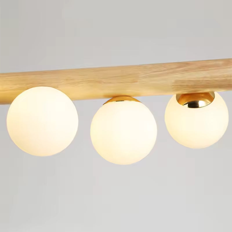 Gros plan sur les globes opalins lumineux fixés à une barre en bois clair, au style naturel, doux et minimaliste.
