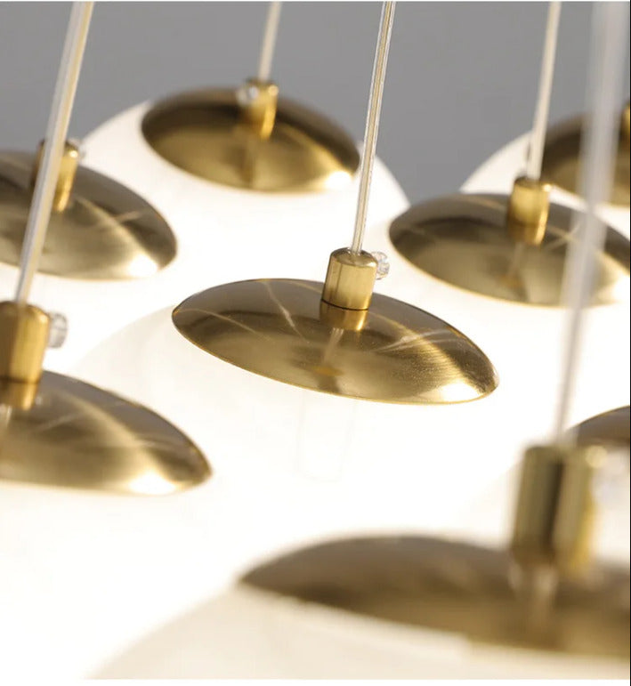 Détail des globes en verre opalin blanc avec capuchons en laiton brossé et câbles fins d'une suspension design.