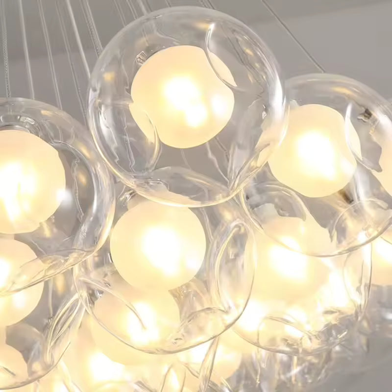 Gros plan sur les bulles de verre transparent d'un lustre sculptural, révélant des sphères lumineuses aux reflets chaleureux.