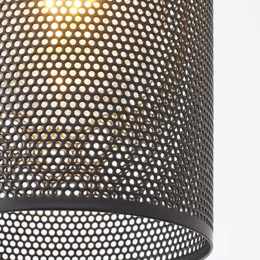 Gros plan sur le métal ajouré noir de la suspension cylindrique, laissant filtrer une lumière chaude et graphique