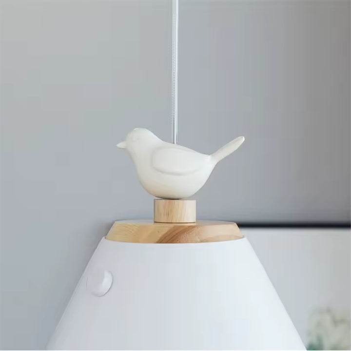 Détail de l’oiseau blanc posé sur une finition en bois naturel, au sommet d’un luminaire conique d’inspiration nordique