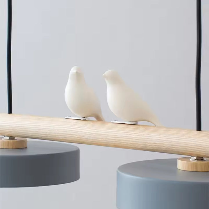Deux oiseaux blancs sculptés reposent sur la barre en bois, apportant une touche poétique au luminaire design