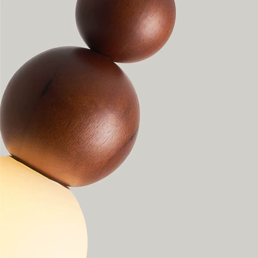 Détail des sphères en bois foncé d’une suspension totem avec globe opalin, au style sculptural et naturel