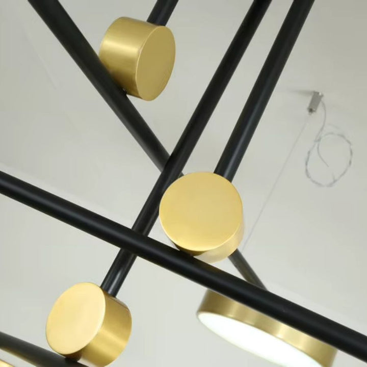 Gros plan sur les croisements de bras noirs et les éléments dorés d’un lustre au design graphique et sculptural.