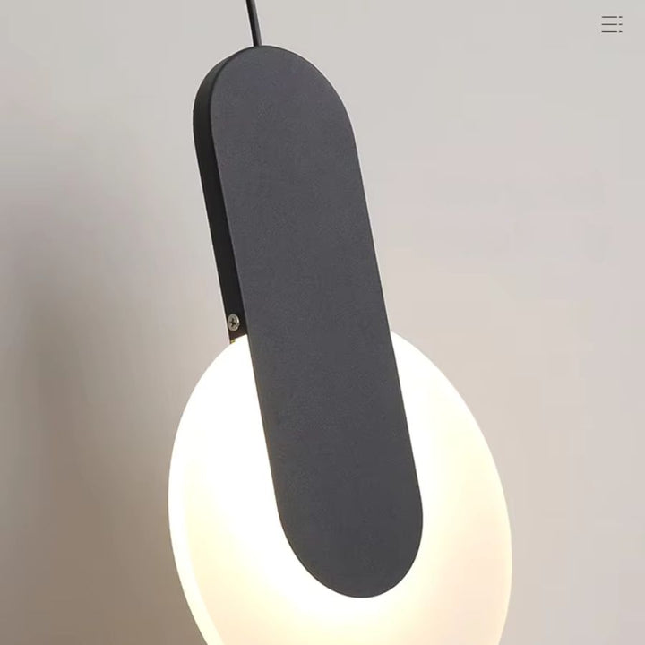 Gros plan sur une suspension disque lumineuse noire à bande verticale au design sculptural et contemporain