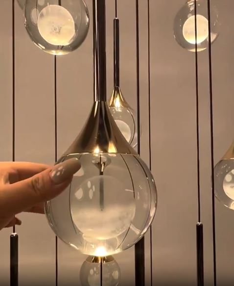 Détail de suspension dorée en verre transparent à cœur opalin, finition élégante style luxe moderne.