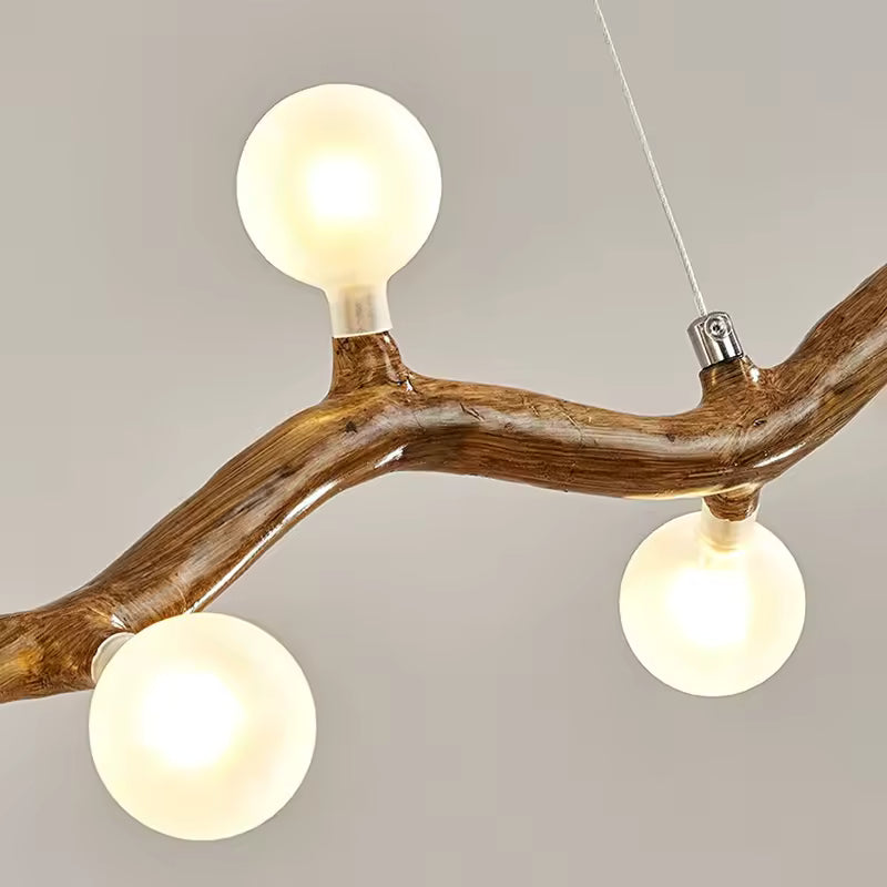 Gros plan sur les globes blancs et la branche courbée effet bois d'une suspension au design naturel et organique.