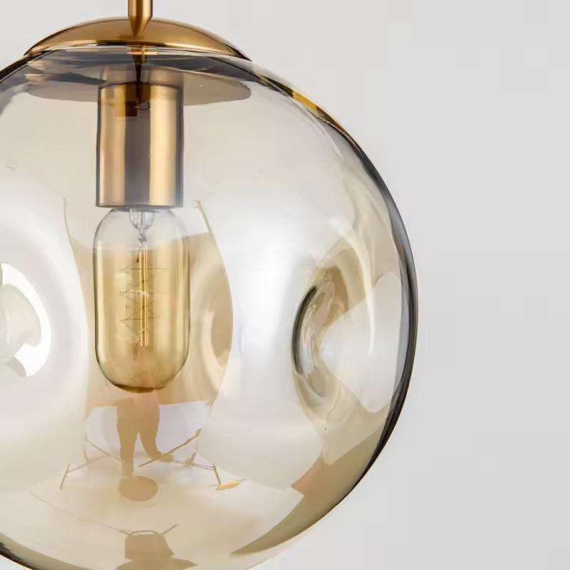Gros plan sur une suspension globe en verre ambré ondulé avec finition dorée, au style vintage chic et décoratif