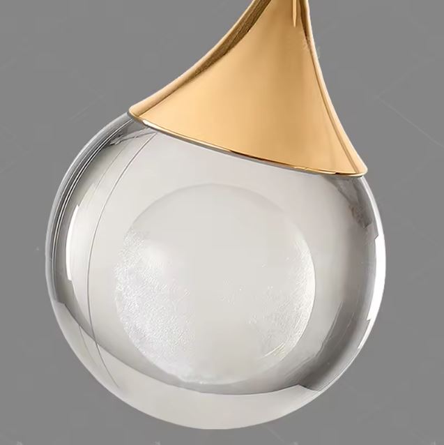 Détail d’une suspension goutte dorée, verre transparent à cœur opalin, style design contemporain chic.