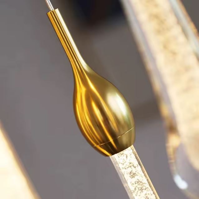 Détail d’une tête de suspension goutte dorée avec tige LED intégrée, soulignant le design raffiné et l’éclat haut de gamme du luminaire.