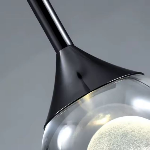 Détail de suspension goutte transparente et noire en verre et métal mat, luminaire design contemporain au style minimaliste chic.