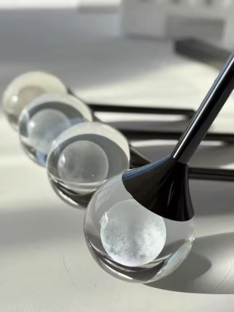 Détail de suspension goutte en verre transparent avec cœur lumineux givré et finition noire, style design minimaliste.