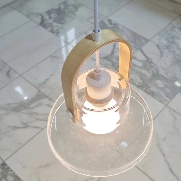 Vue rapprochée du luminaire en frêne naturel et verre soufflé transparent, avec poignée courbe et globe lumineux