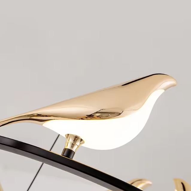 Détail raffiné d’un oiseau lumineux doré monté sur anneau noir, pour suspension sculpturale au style poétique et décoratif contemporain.