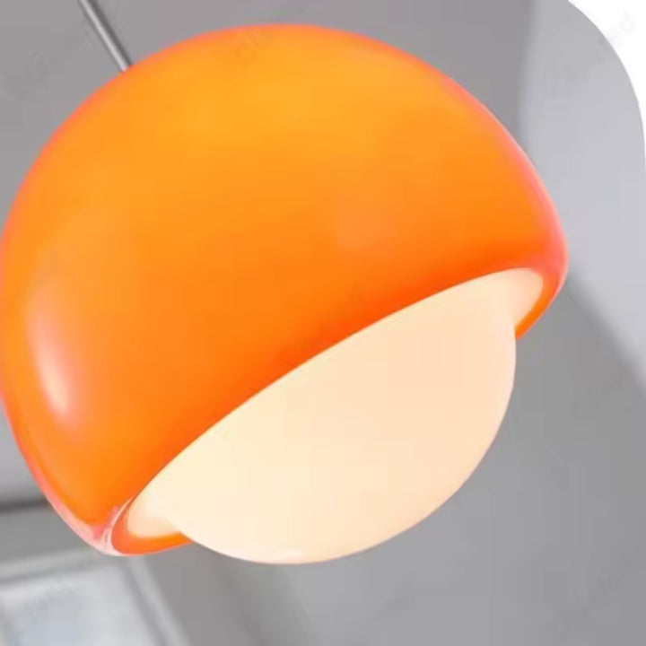 Gros plan sur une suspension orange au design rétro, associant dôme brillant et globe opalin lumineux