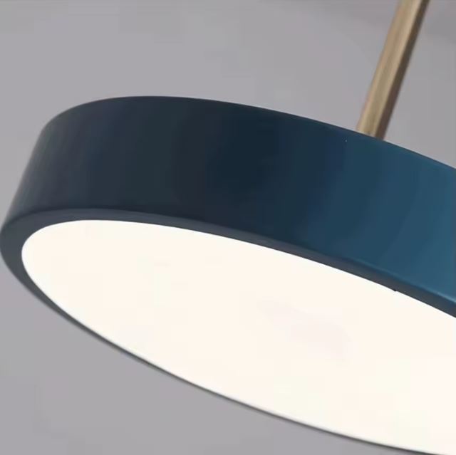 Gros plan sur le design moderne d'une suspension plate bleue avec une tige dorée et un éclairage doux.