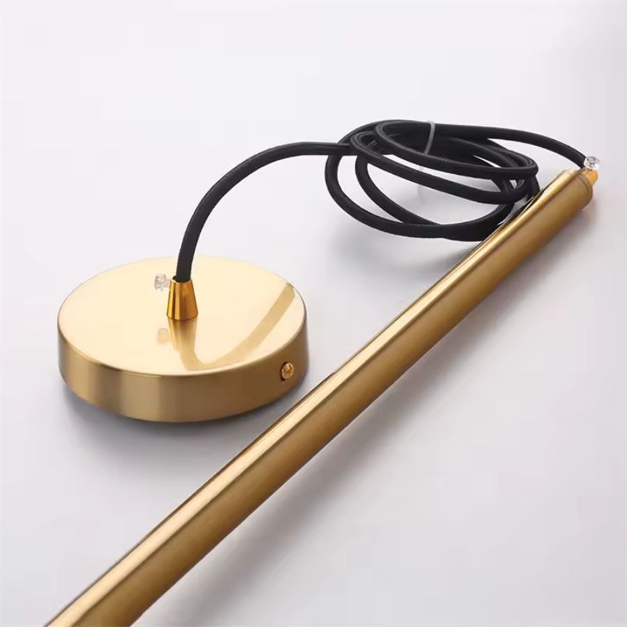 Détail de la suspension en métal doré avec rosace ronde et tube élancé, dans un style minimaliste et contemporain