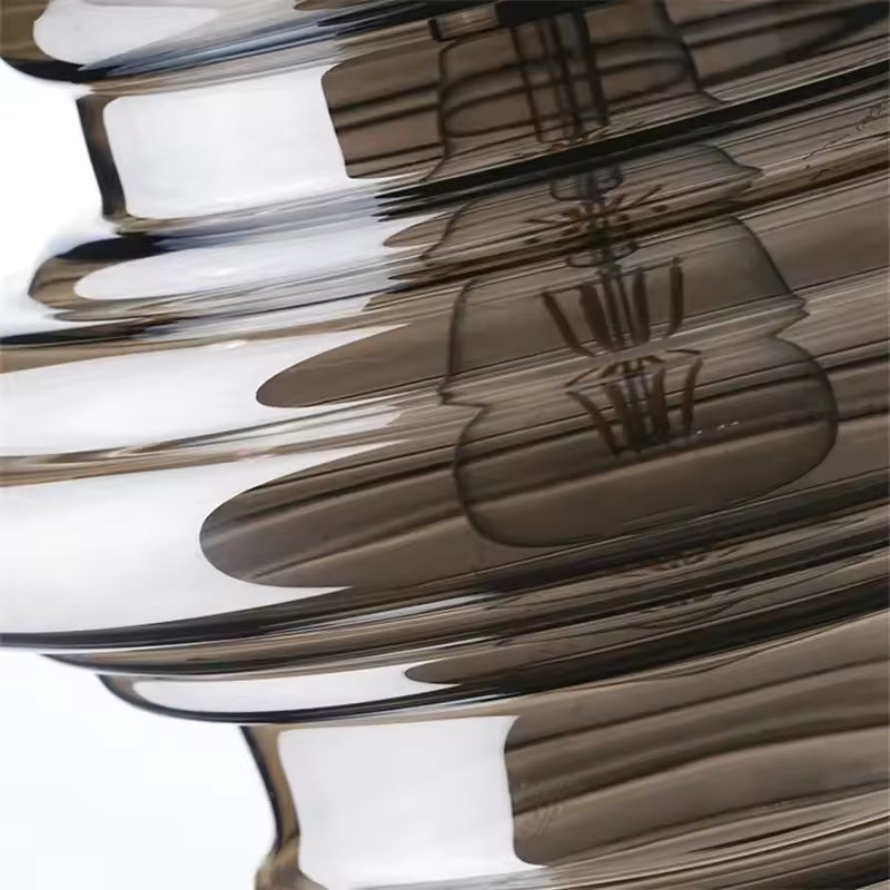 Gros plan sur les reliefs ondulés d'une suspension en verre fumé, aux courbes superposées et reflets élégants.