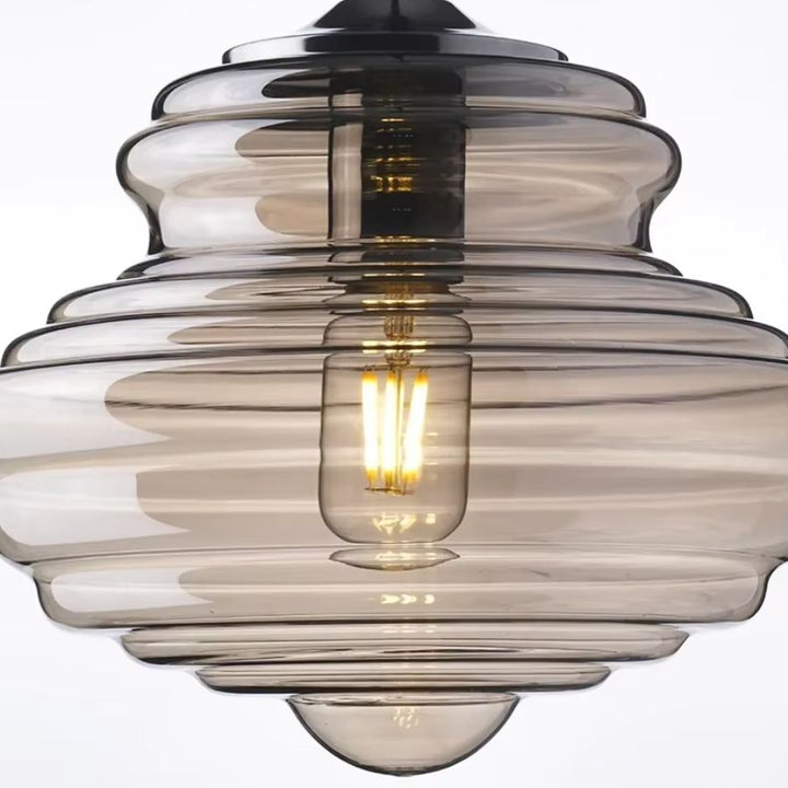 Gros plan sur une suspension en verre fumé aux reliefs étagés, avec ampoule à filament et design sculptural rétro.