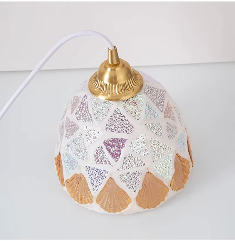 Détail de la suspension en verre façonné irisé, ornée de coquillages dorés et d’une monture au charme vintage