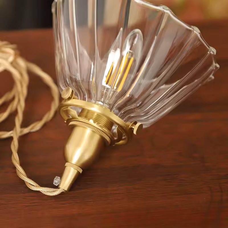 Vue rapprochée d’une suspension vintage en verre strié et laiton, avec câble tressé au charme rétro