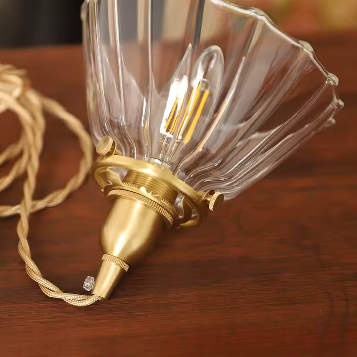 Vue rapprochée d’une suspension vintage en verre strié et laiton, avec câble tressé au charme rétro