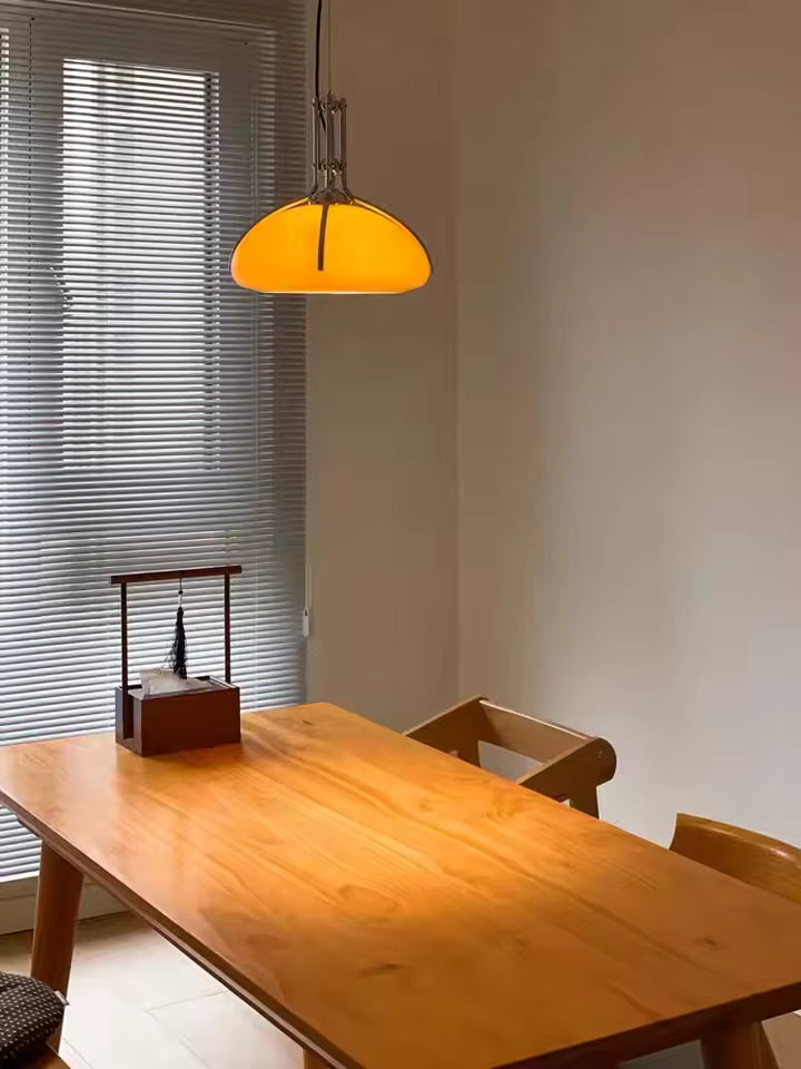 Luminaire orange en forme de dôme au-dessus d’une table en bois, avec détails chromés et esthétique Space Age rétro