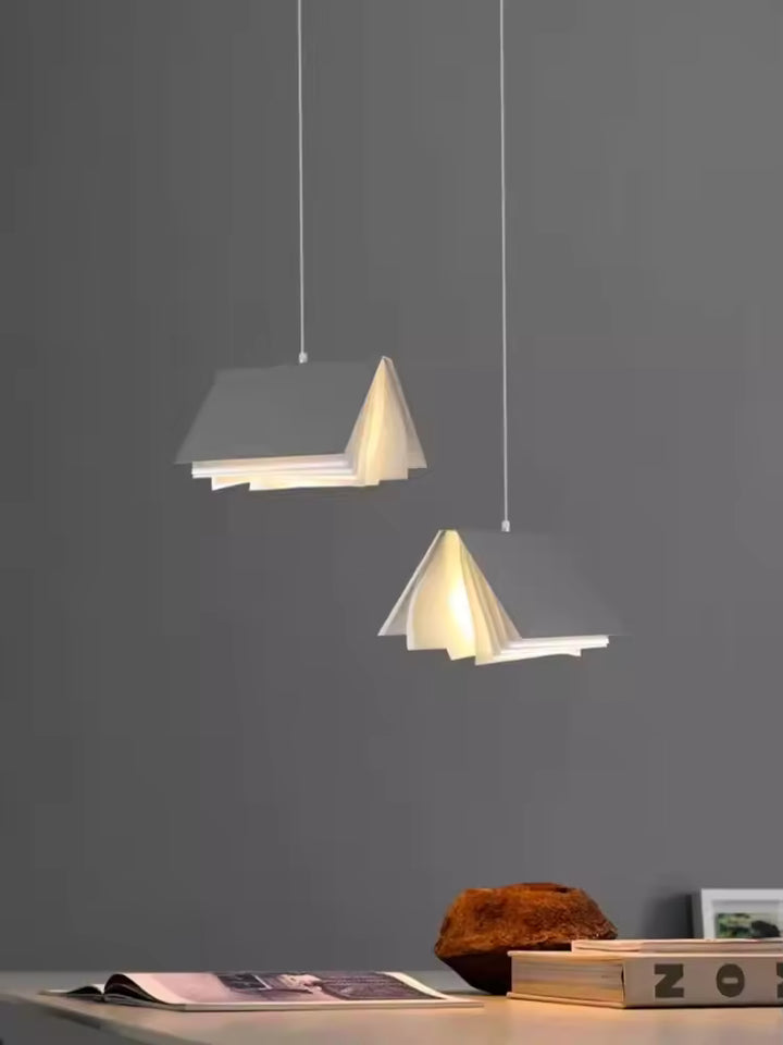 Deux suspensions design en forme de livre ouvert diffusant une lumière chaude dans un décor moderne et épuré